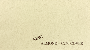 Text on a textured almond-colored paper reads "NEW! ALMOND – C240 COVER" in dark brown font, indicating a new product or material sample.